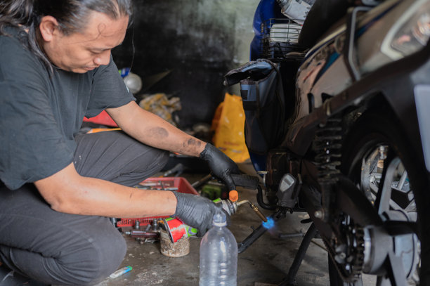 亚洲马来男性机械师使用手电筒加热摩托车零件进行修理的库存照片图片下载
