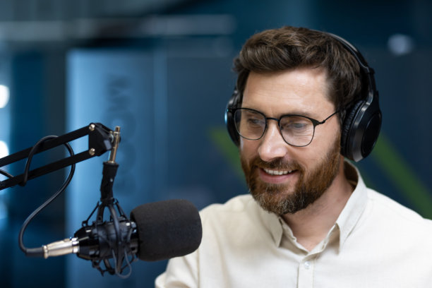 年轻微笑的男子戴着耳机，坐在室内对着麦克风讲话的特写照片图片下载