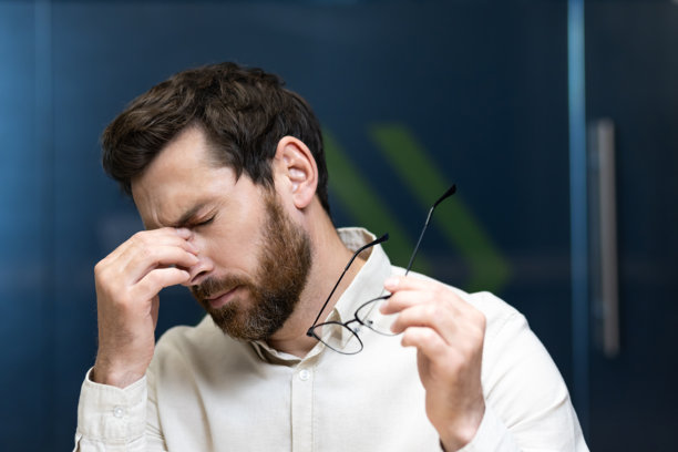 年轻商人在办公室疲惫地坐着，手中拿着眼镜，揉着眼睛的特写照片图片下载