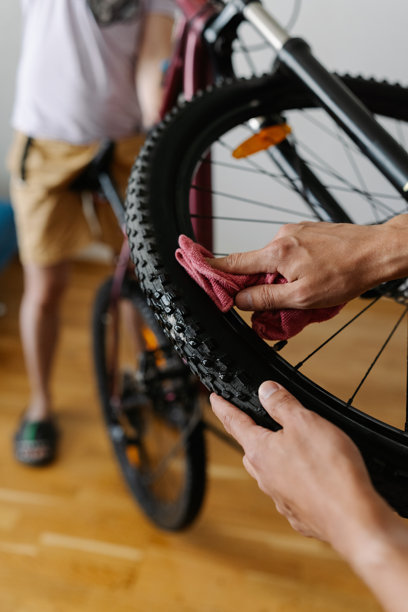 垂直裁剪的照片，骑自行车的人在车间用布清洁自行车轮胎，确保最佳性能并保持自行车的完美状态，特写镜头。图片下载