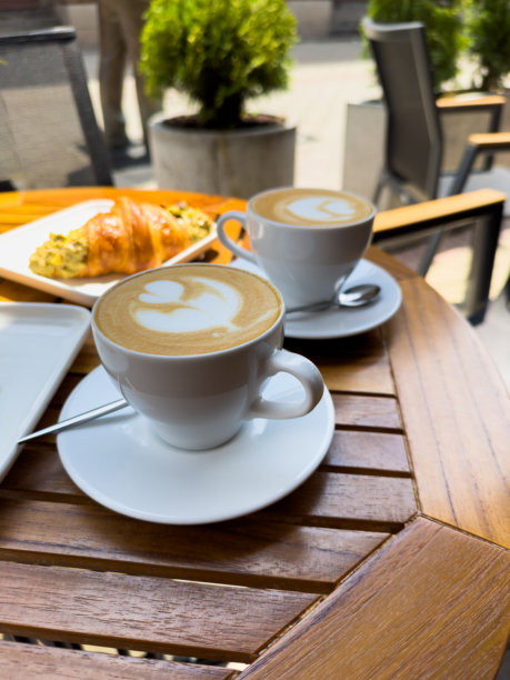 一只白色的卡布奇诺咖啡杯放在木桌上，旁边是一盘可颂。巴黎早晨的咖啡馆早餐，欧洲的早晨。竖版照片图片下载