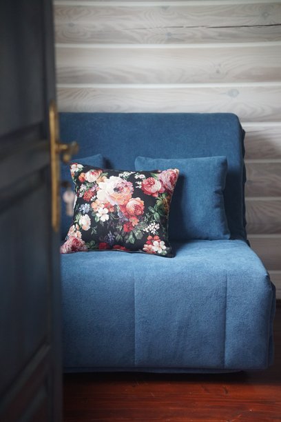 一个舒适的乡村风格房间内部，配有柔和的蓝色沙发和装饰性的花卉抱枕。温暖而宁静的氛围，背景是木质墙壁，自然光线和复古魅力。图片下载