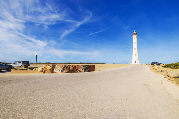 阿鲁巴的加州灯塔，附近墙壁上有猫头鹰壁画，沙滩路在晴朗的蓝天下。图片下载