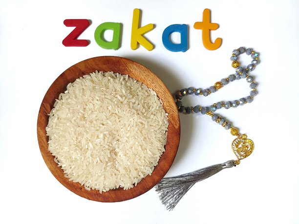 一碗米饭，五彩字母的“ZAKAT”字样和祈祷珠或念珠，背景为白色。图片下载