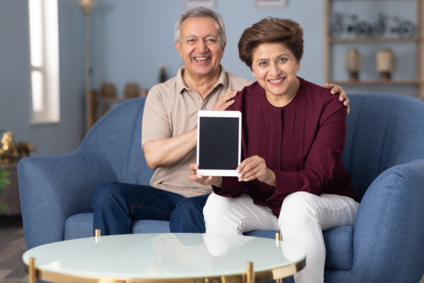 老年夫妇坐在家里的沙发上展示设备屏幕的照片图片下载