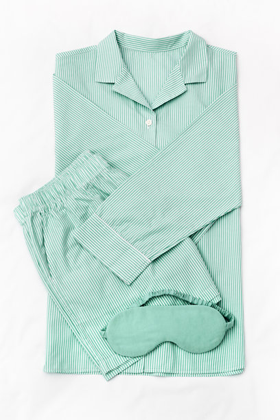 从上方俯视折叠的条纹绿色女式睡衣和白色床上的缎面睡眠眼罩。简约的平铺舒适睡衣，适合睡眠和放松。时尚睡衣的美学生活方式照片。图片下载