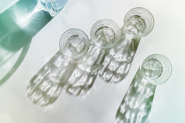 透明水杯和水壶在阳光下的白色背景上投下阴影，简约风格的柔和色调照片，俯视角度下闪亮的杯子在自然光下闪烁，夏季饮品，构图。图片下载