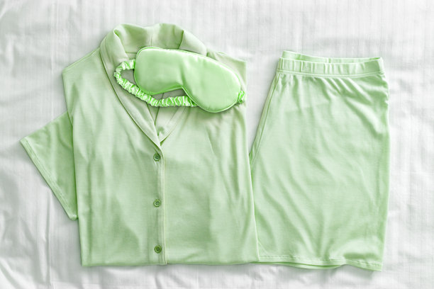 俯视折叠的淡绿色女性睡衣和白色床上的缎面睡眠眼罩。简约的舒适睡衣平铺，适合睡觉和放松。时尚睡衣的美学生活方式照片。图片下载