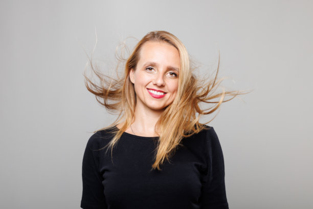 一位长发飘逸的女商人自信地微笑，背景为灰色，在一次宣传照片拍摄中展现了她充满活力的个性和职业精神。图片下载