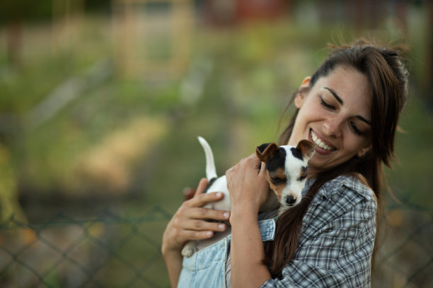 年轻女性农民在花园里温柔地抱着一只小狗。库存照片图片下载