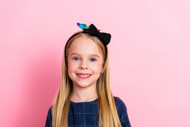 穿着可爱发带的快乐小女孩站在粉色背景前，散发着幸福和时尚感图片下载