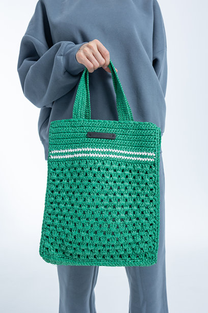 美丽的模特外貌女性。穿着灰色卫衣、手提绿色包的女孩，背景为浅色。时尚妆容的漂亮女性在摄影棚中摆姿势。竖版照片。图片下载