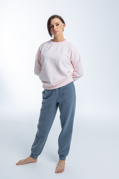 美丽的模特外貌女性。女孩穿着浅粉色毛衣和灰色裤子，背景为浅色。时尚妆容的漂亮女性在摄影棚中摆姿势。竖版照片。图片下载