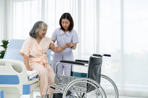 一名护士把一名亚洲老人扶上轮椅，带他去给他在事故中受伤的腿拍x光片。图片下载