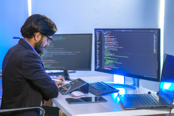 一位专注的亚洲金融分析师或软件开发人员在现代办公室加班，监控多个屏幕上的数据。金融科技、数据分析和网络安全的概念。图片下载