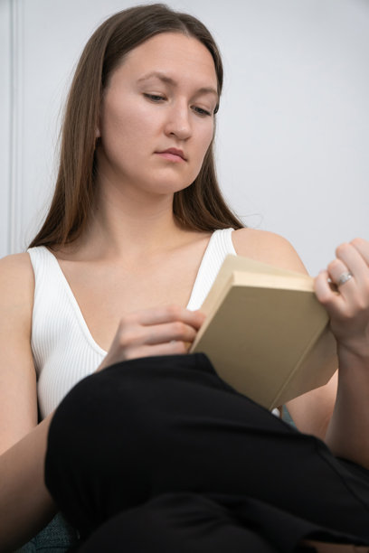 年轻女性在家中舒适地坐在沙发上阅读一本书，享受宁静的休闲时光，沉浸在文学中。竖版照片图片下载