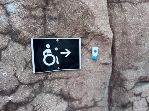 无障碍标志，带有轮椅图标和箭头，安装在纹理石墙上，旁边是服务按钮，指示方向并为公共环境中行动不便的人士提供支持呼叫。图片下载