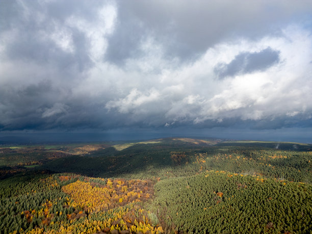 高空俯瞰一片浓密的混合森林，秋季的树叶在起伏的山丘和山谷下燃烧着，天空云层变幻，适合自然和旅行项目的高分辨率库存照片。图片下载