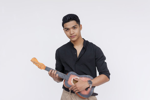 一位年轻英俊、衣着考究的亚洲男性在演奏尤克里里。全身照片，背景为白色。图片下载