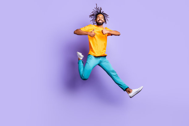 乐观的棕发男士穿着黄色T恤，竖起大拇指，背景为紫色，照片为全身照。图片下载