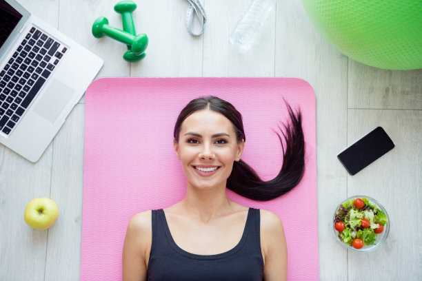 高角度俯视照片，年轻迷人的女性躺在垫子上，面带快乐积极的微笑，展现运动健康的室内氛围。图片下载