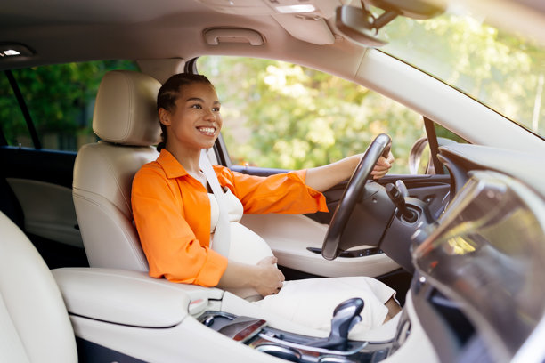 年轻的非裔美国孕妇快乐地开车，手放在肚子上图片下载