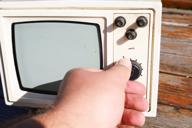 一只人手在木质表面上调整一台旧便携式电视的设置。这张照片强调了与复古科技的互动，唤起了对过去时代的怀旧情感。图片下载