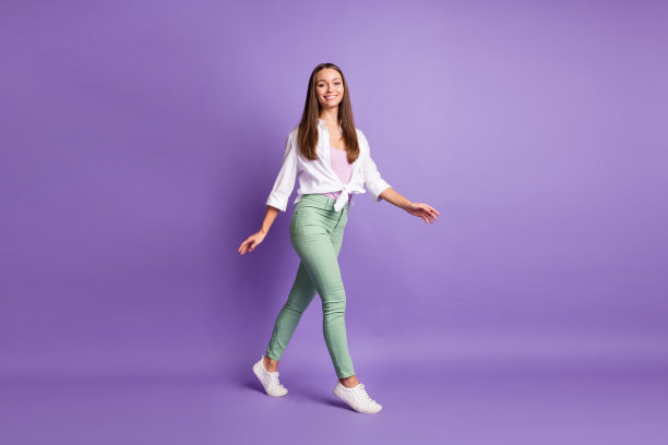 女孩穿着运动鞋、长裤和白衬衫，走路的全身照片，背景为紫色。图片下载