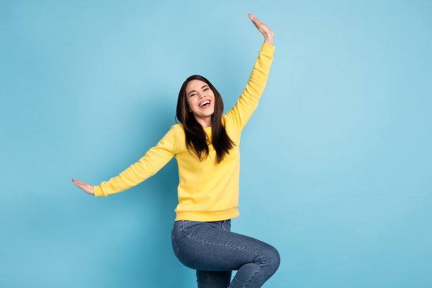 穿着黄色衬衫的乐观棕发长发女士在明亮的蓝色背景上跳舞的照片图片下载