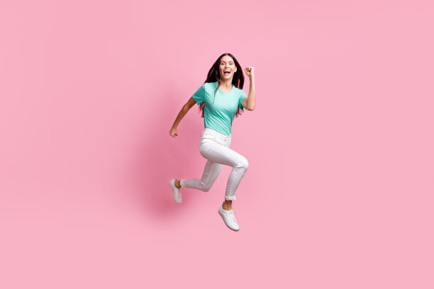 年轻美丽可爱快乐疯狂微笑的女孩在粉色背景上奔跑的全身侧面照片图片下载