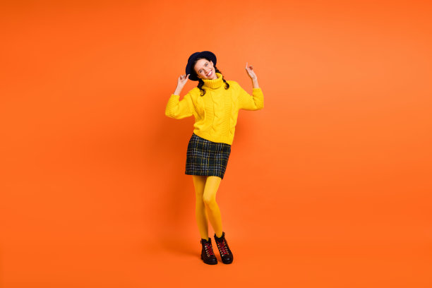 充满活力的女孩穿着黄色毛衣、短裙和鞋子在橙色背景上跳舞的全身照片图片下载