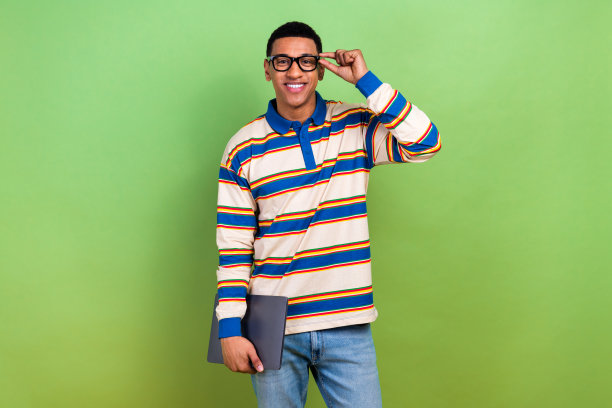 时尚年轻男士的照片肖像，穿着条纹服装，佩戴眼镜，正在使用笔记本电脑，背景为绿色。图片下载