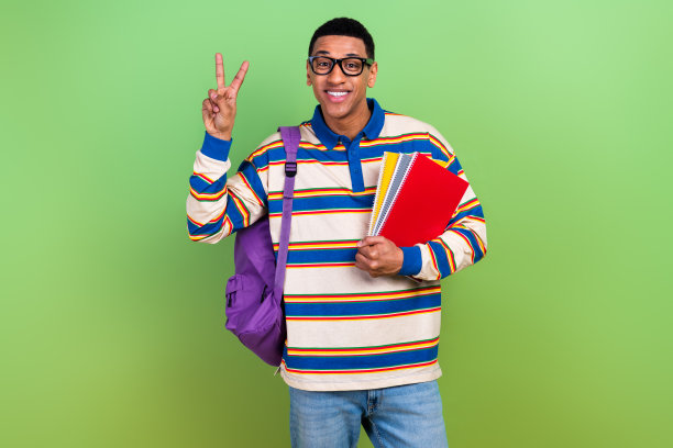 帅气的年轻大学生在绿色背景下穿着时尚条纹服装，做出V字手势的照片肖像图片下载