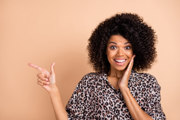 惊讶女孩的照片肖像，触摸脸颊，指着空白区域，建议，背景为柔和的米色。图片下载