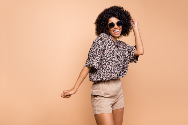 周末穿着豹纹衬衫的女人戴着太阳镜在淡米色背景下跳舞并大笑的照片肖像图片下载