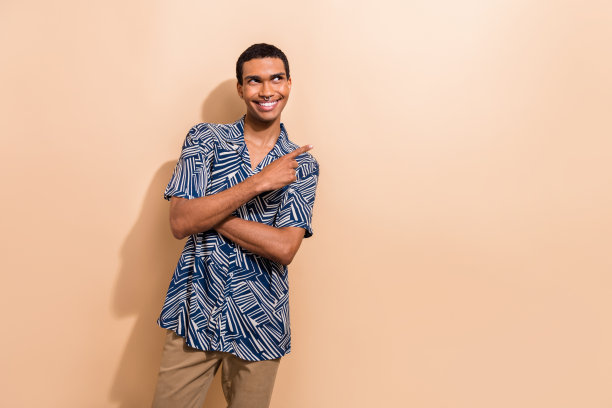 时尚蓝色印花服装的帅气年轻男士在米色背景前指向空白处的照片肖像图片下载