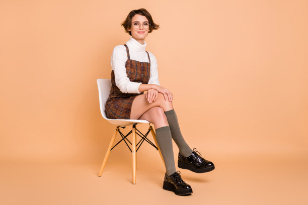 乐观的短发女孩穿着裙子、袜子和鞋子，坐在桃色背景上，照片为全身照。图片下载