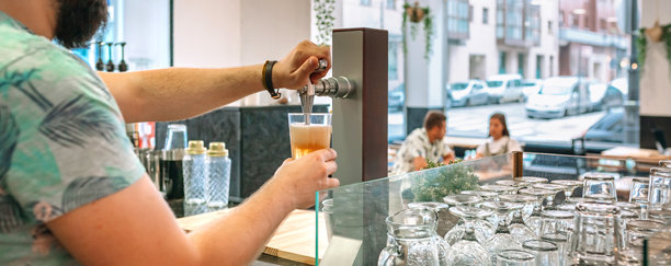 无法辨认的酒保在酒吧里从龙头倒啤酒，背景是坐着顾客的餐厅。图片下载