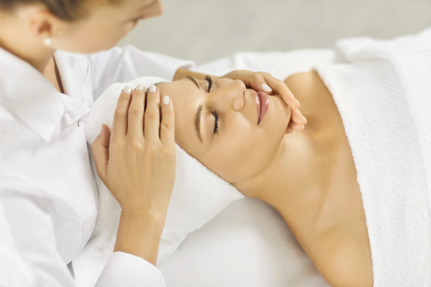 特写照片，漂亮的年轻女性躺着，闭着眼睛，在水疗中心享受面部或头部按摩。图片下载