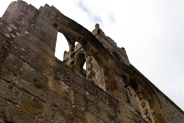 一张向上拍摄的历史钟楼风化石材的照片，背景是多云的天空。图片下载
