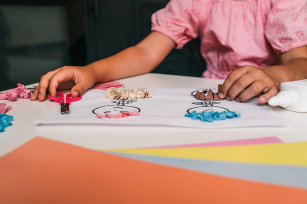 孩子正在用绘画、彩色纸、胶水和剪刀制作纸艺项目。这是一项动手的教育活动，使用明亮的粉彩纸和富有创意的卡通面孔的纹理发型。图片下载