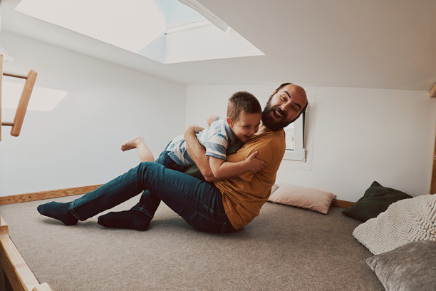 父亲和儿子的照片。他们在小房子的卧室里玩摔跤。图片下载