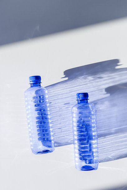 清晰塑料水瓶在白色蓝色背景上的特写，简约美学生活照片，俯视图，平铺，自然光，阳光阴影，光线折射效果，星形滤镜图片下载