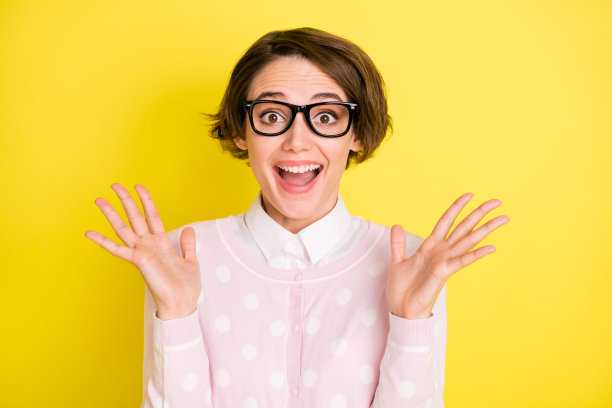 戴着眼镜的快乐女孩在鲜艳的黄色背景下惊讶地做出胜利手势的照片肖像图片下载