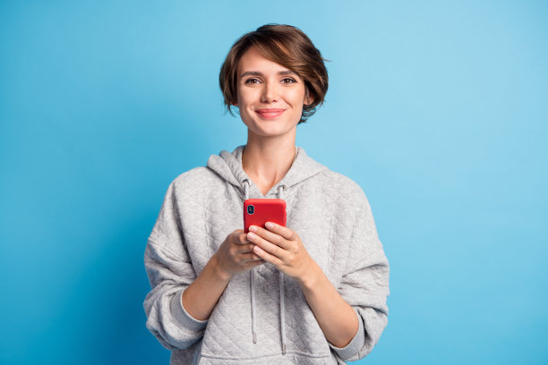 女性学生微笑着在鲜艳蓝色背景下用手机发送信息的照片肖像图片下载