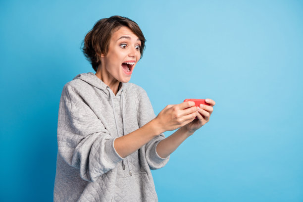 兴奋的女学生在鲜艳的蓝色背景下玩手机游戏，惊讶的照片肖像图片下载
