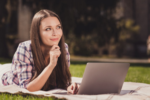 梦幻而沉思的女孩在草地上微笑着使用电脑学习的照片肖像图片下载