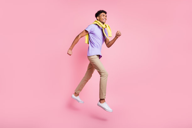 年轻帅气的非洲裔男子在粉色背景上微笑着奔跑的全身侧面照片图片下载