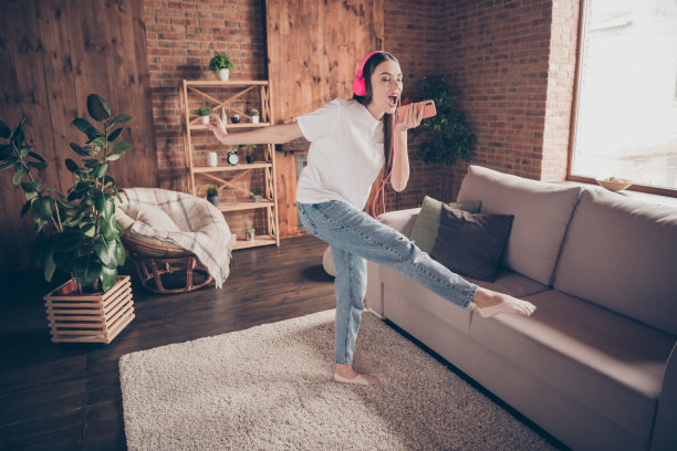 年轻女性全身侧面照片，快乐积极，微笑着跳舞，戴着耳机，唱歌，手持智能手机，室内环境。图片下载