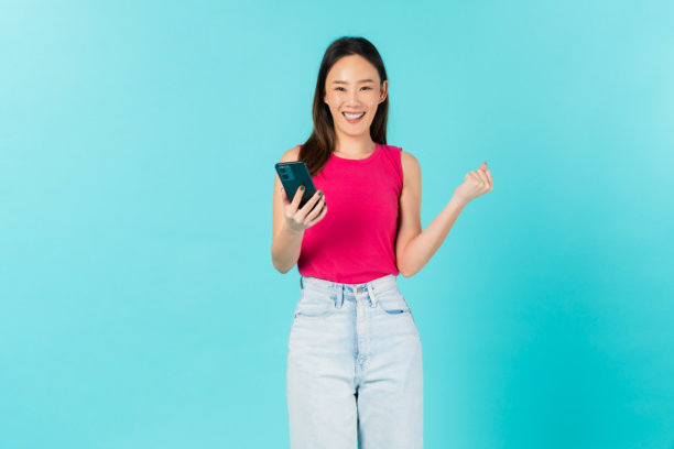 美丽的亚洲女性在蓝色背景下微笑着拿着智能手机的工作室拍摄照片。图片下载